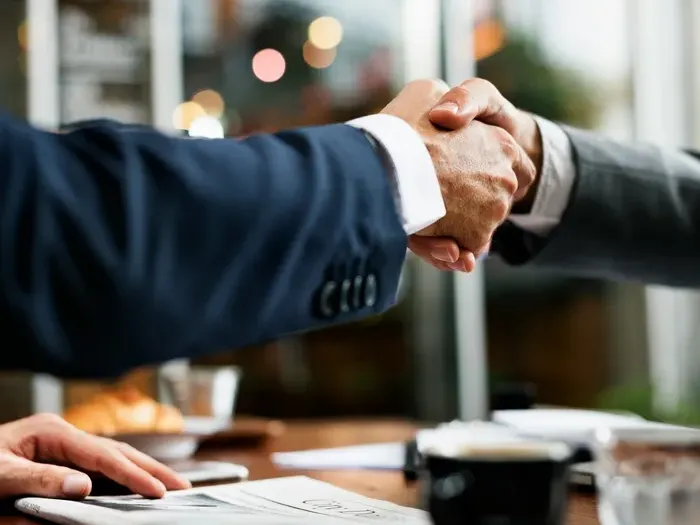 Two professionals shaking hands at a table, showing partnerships and helpful services in the city directory